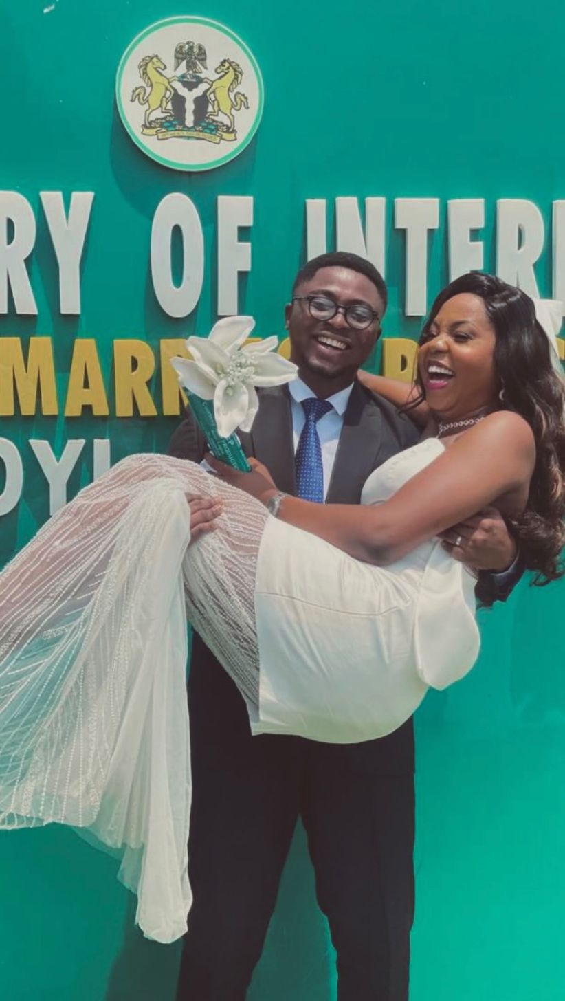 Groom carrying a laughing bride in an Aidoo dress at the marriage registry